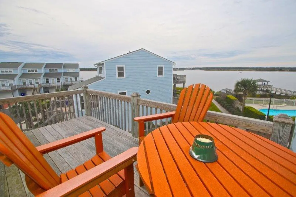 A scenic view from a private deck, showcasing orange Adirondack chairs and a wooden table overlooking the water. The tranquil setting is ideal for enjoying sunsets or a quiet morning coffee.