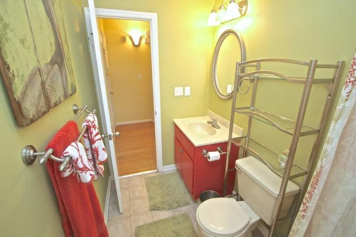 A brightly lit bathroom with a cheerful red vanity, round mirror, plush towels, and a shower curtain. The atmosphere is fresh and inviting, ideal for both quick refreshes and soothing baths.