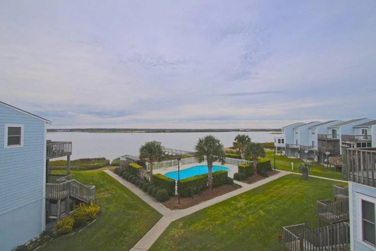 A peaceful view of the community pool set against a scenic waterfront, surrounded by palm trees and a landscaped garden. The calm atmosphere is perfect for both relaxation and family swims after a day at the beach.