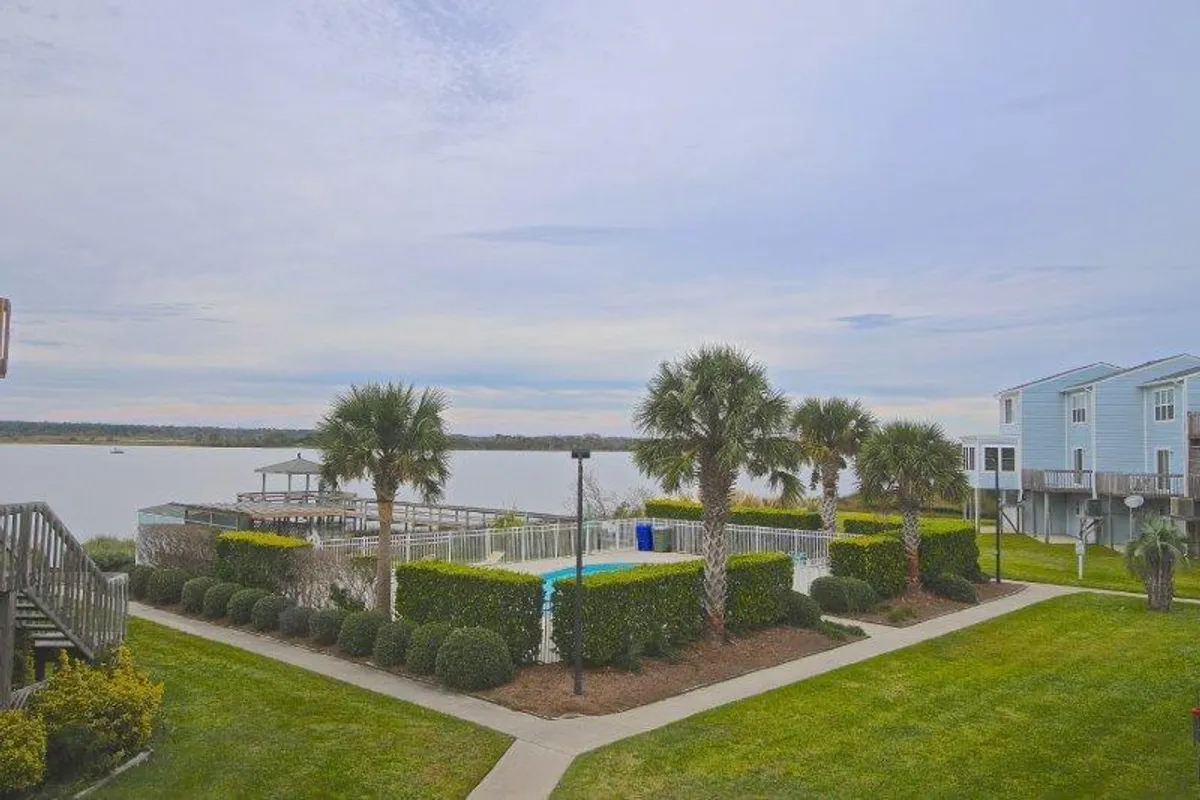 An inviting view of the community pool area set against a picturesque waterfront with landscaped gardens and palm trees. The scene hints at the possibility of sunset views and peaceful swims, encapsulating the sense of relaxation and vacation ambiance at Bermuda Landing.