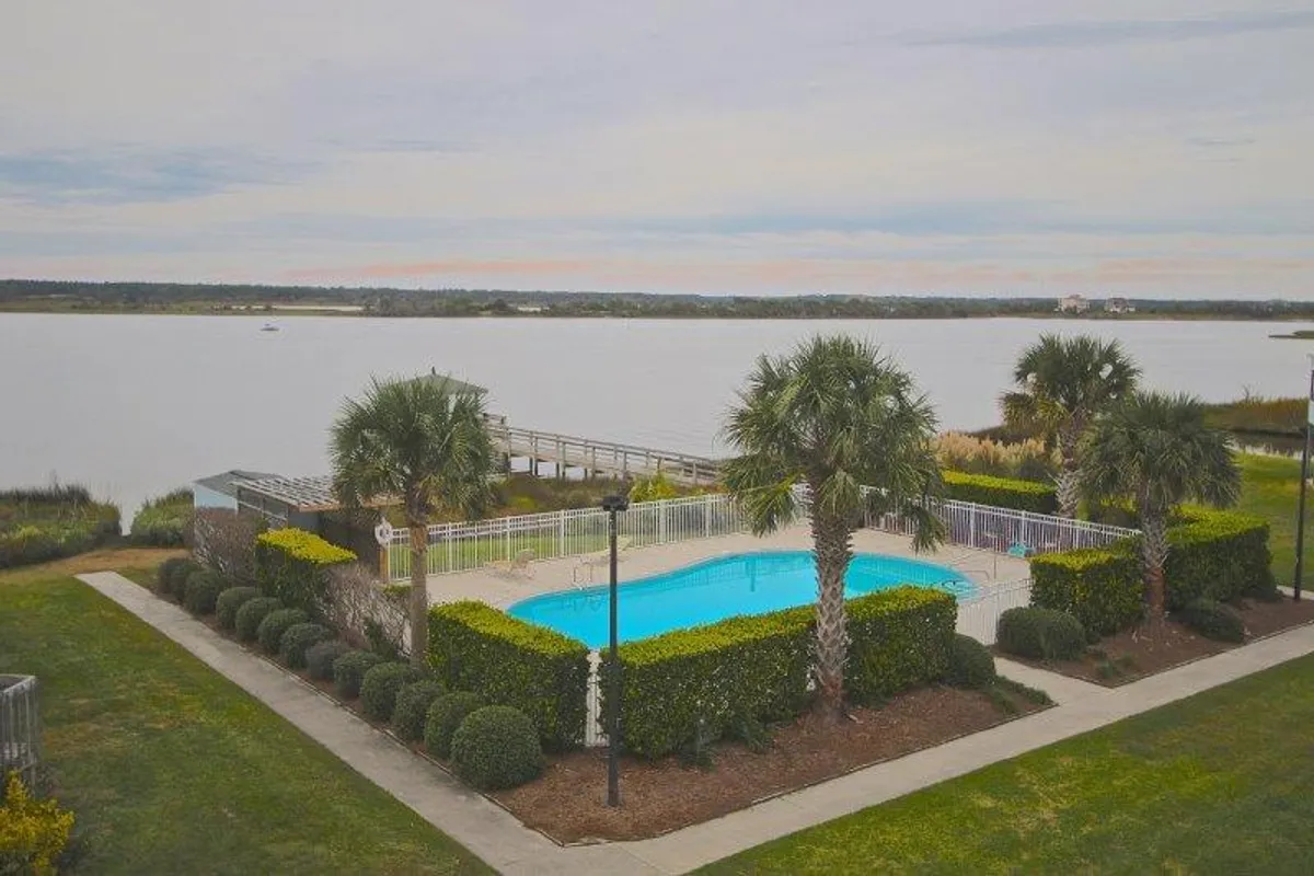 A serene outdoor scene showcasing the sparkling community swimming pool surrounded by palm trees, with a dock extending over the water. The tranquil atmosphere is enhanced by the waterfront backdrop and inviting poolside area, suggesting a perfect spot for relaxation and social gatherings.