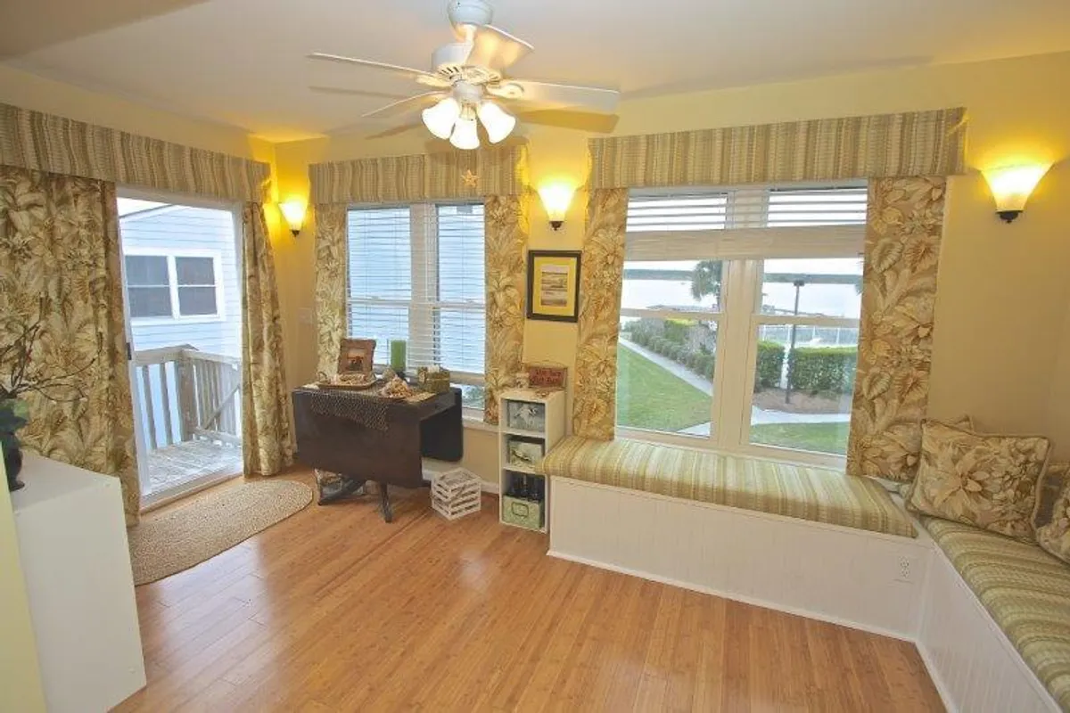 This image showcases a sunlit interior corner with large windows, decorative window seating, and a small desk adorned with cozy decor. Natural light pours into the inviting nook, making it ideal for reading, enjoying a drink, or simply relaxing in peaceful surroundings.