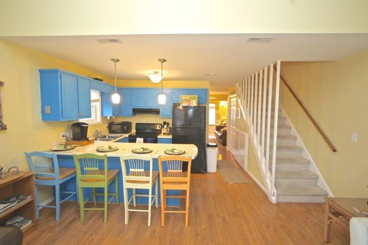 This image showcases a vibrant kitchen with colorful bar stools, a spacious island, and bright blue cabinets. The large island invites group meal preparation and doubles as a casual gathering spot, while the cheerful decor adds a welcoming, budget-friendly vibe.