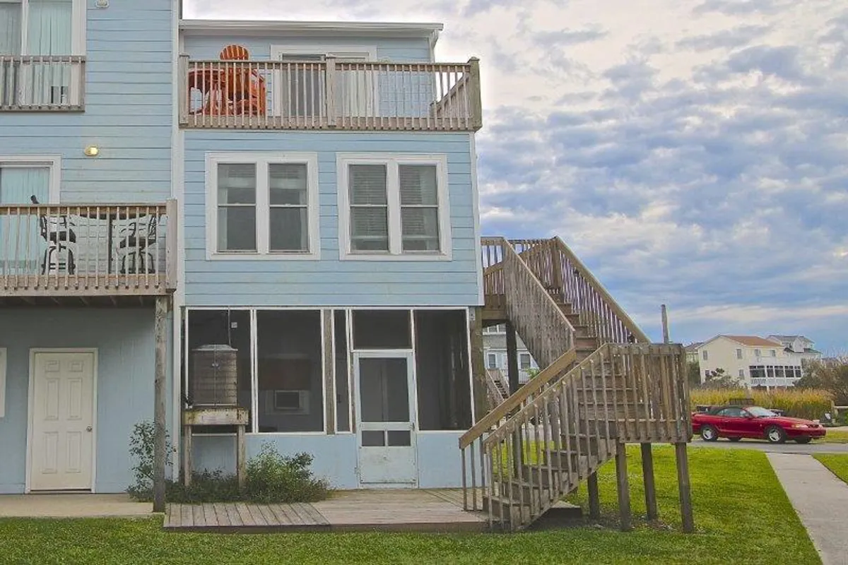 This exterior image showcases an inviting home with prominent balconies, a staircase, large windows, and comfortable outdoor furniture. The balconies overlook the surrounding area, offering unobstructed views perfect for enjoying sunsets, relaxing, or sharing time together. The mood is warm and welcoming, ideal for couples seeking a peaceful retreat.
